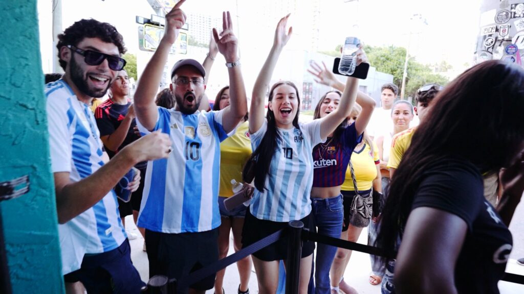 Argentina soccer fans in Messi #10 jerseys cheer with arms raised at the entrance of Grails Miami on a sunny day at Grails in Miami