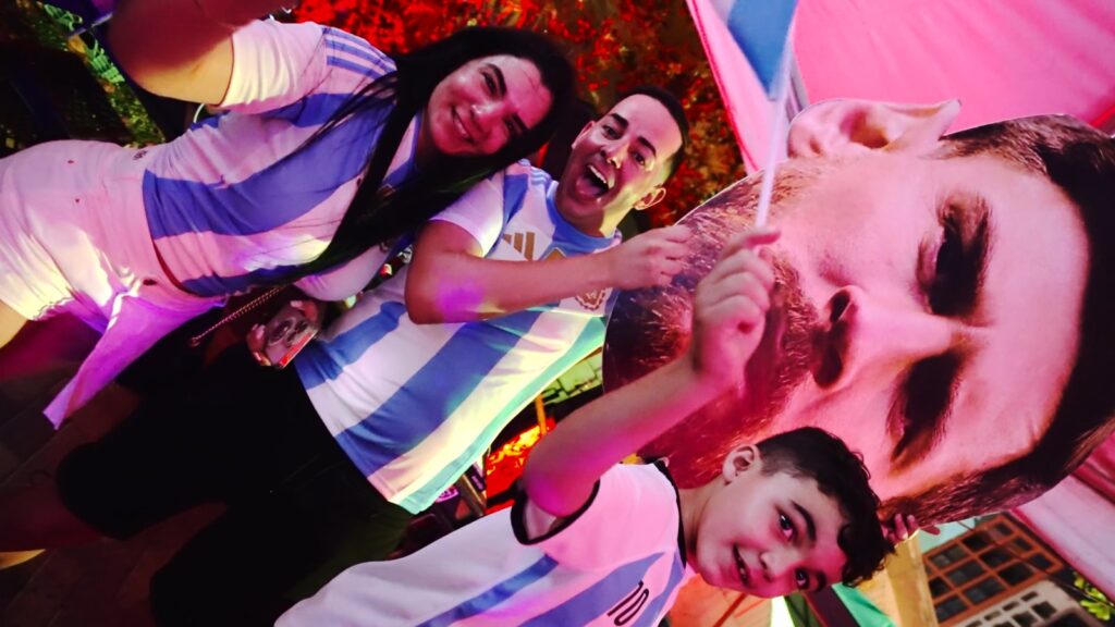 Argentina fans in albiceleste jerseys pose with a life-size Lionel Messi cardboard cutout at Grails Miami watch party