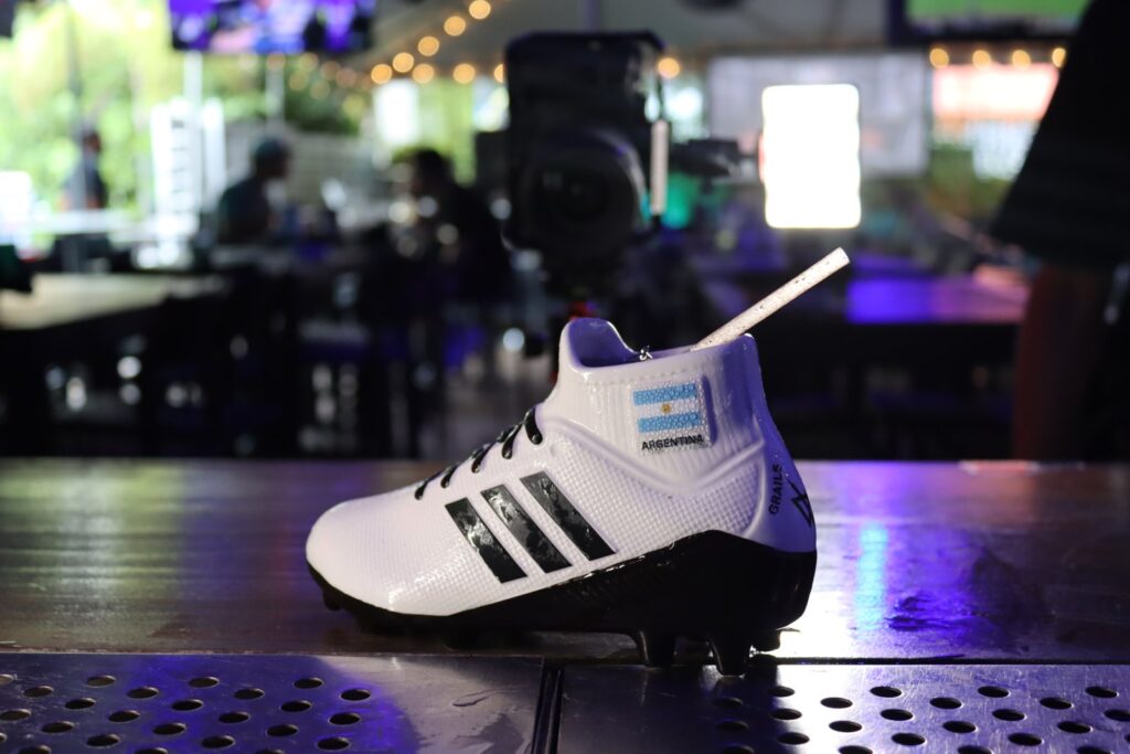 Signature Grails cocktail served in an Argentina-branded Adidas soccer cleat glass on the bar counter