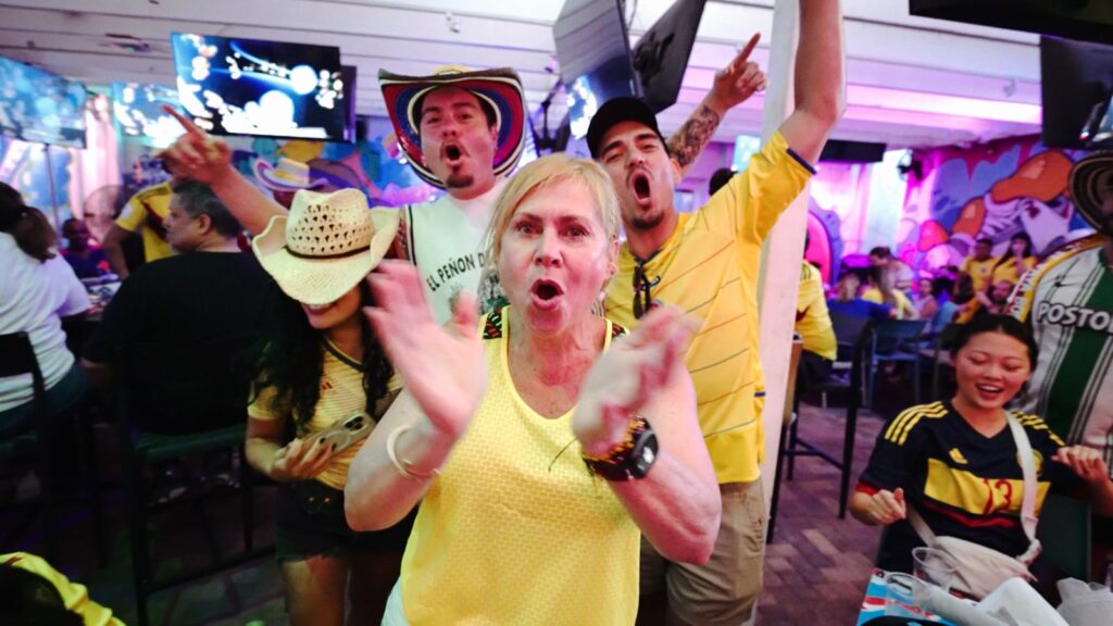 Colombia soccer fans in yellow jerseys cheer and clap during a watch party at Grails Miami, with one wearing a traditional vueltiao hat.