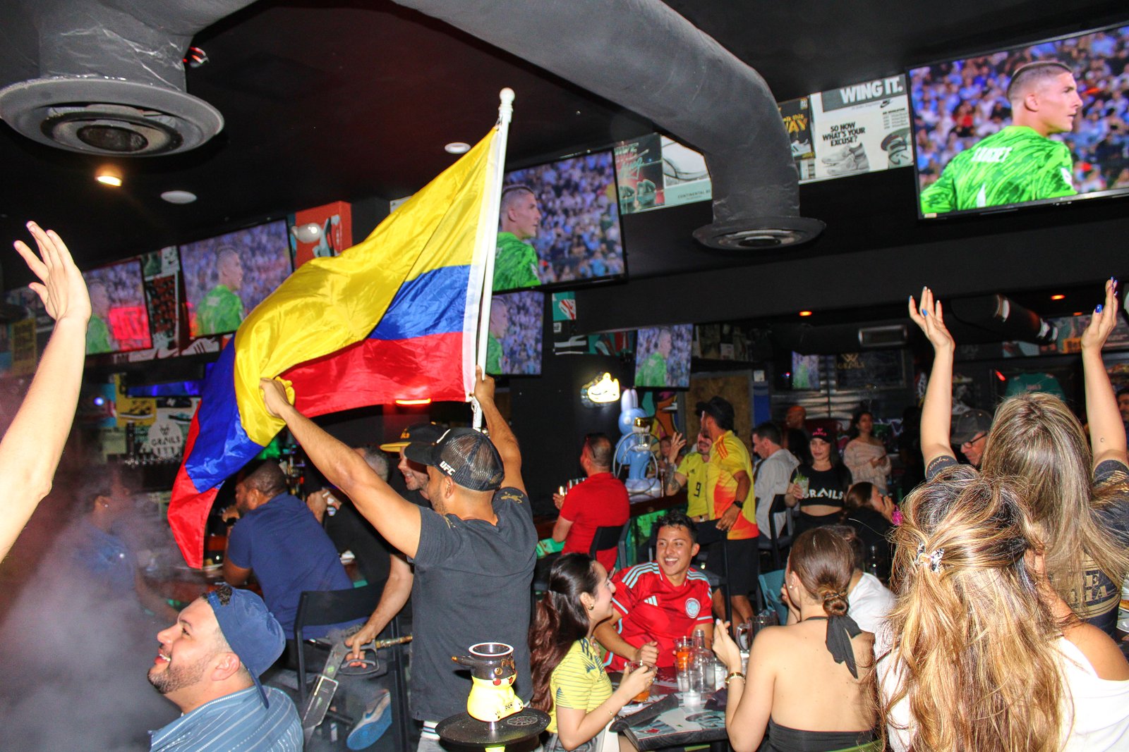 Colombia fans wave a Colombian flag and cheer with arms raised during a soccer watch party at Grails Miami.